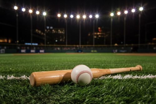 Baseball and bat on the grass of a baseball field at night