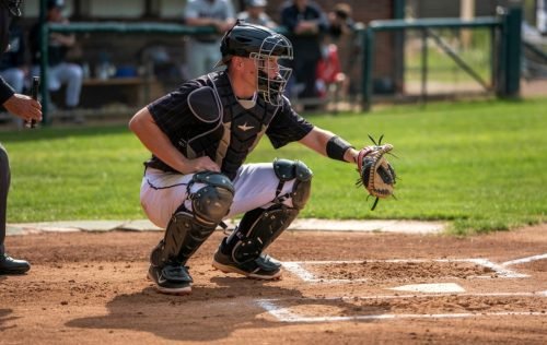 Baseball catcher in full gear crouches, glove extended, ready for a pitch