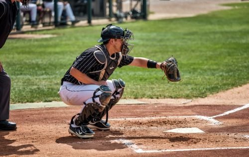 Baseball catcher in gear crouches, reaching for a pitch at home plate