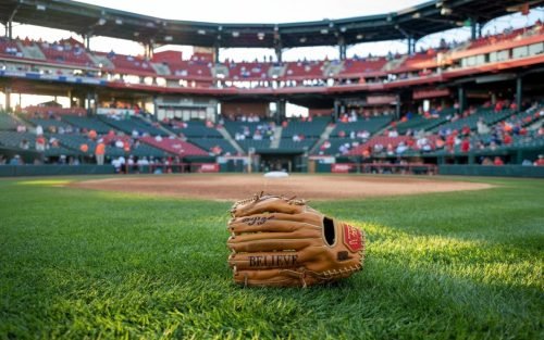 Baseball glove on the grass field with Believe in front of a stadium