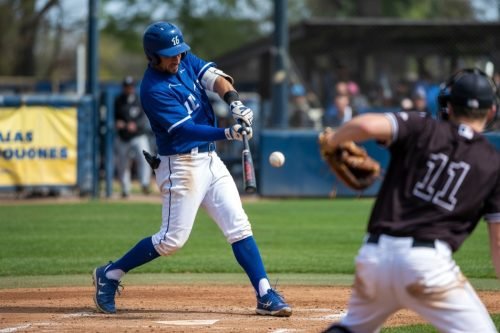 Baseball player in blue uniform swings bat as ball flies toward catcher