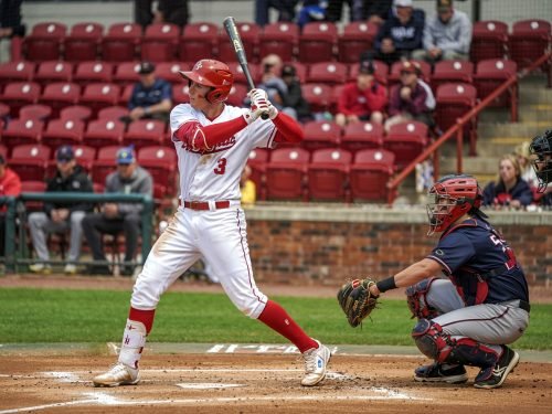 Baseball player in red uniform swings bat, catcher crouches in front