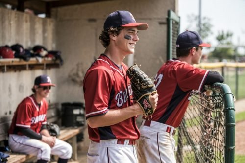 Baseball players in red uniforms stand in a dugout, smiling and holding gloves