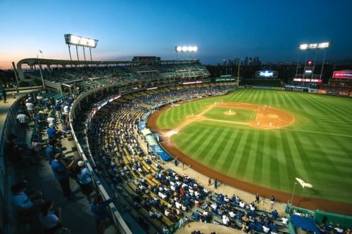 Baseball stadium at dusk, filled with fans, illuminated by stadium lights