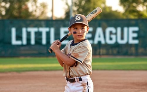 Young baseball player at bat, wearing a uniform, with Little League in background