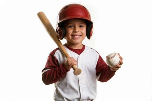 Young baseball player in uniform, holding bat and ball, smiling