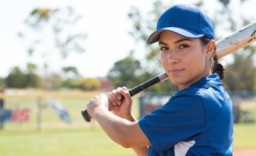 Young woman in baseball uniform holding a bat, looking at the camera